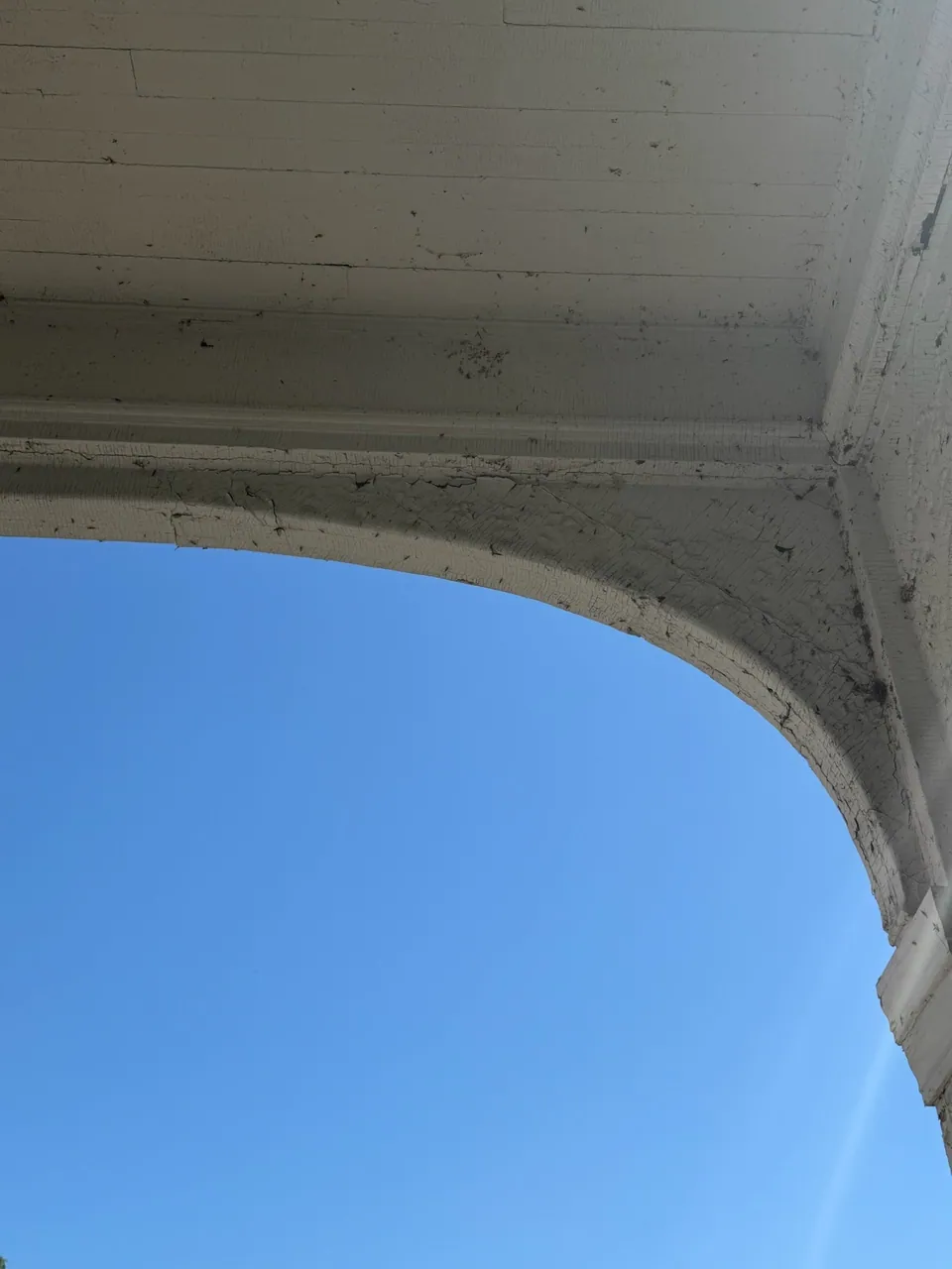 The underside of the porch arch and its ceiling in cracked white paint, against a blue sky.