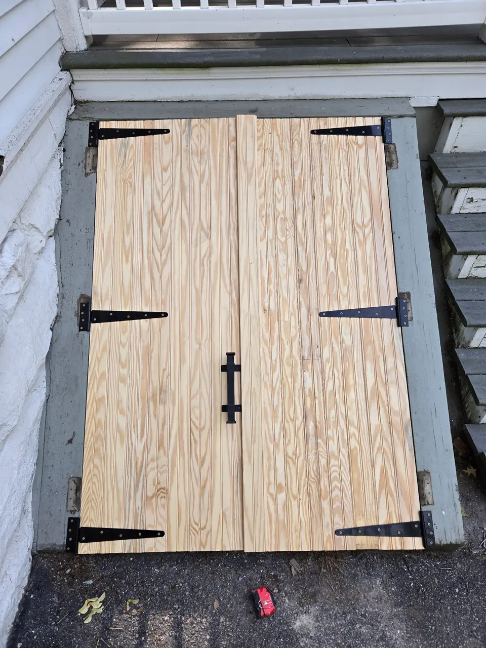 The new cellar doors in bare beadboard pine with black strap hinges and a black handle.